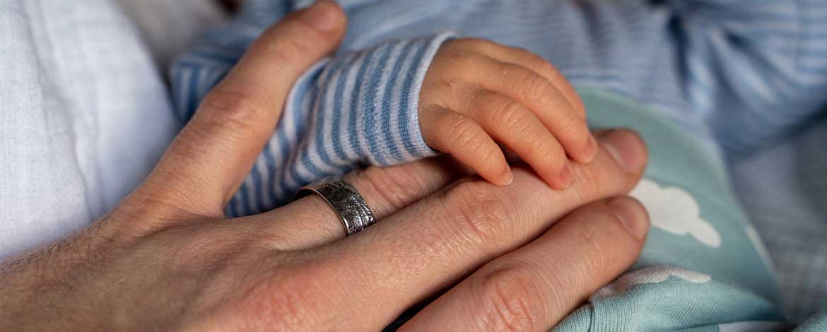 a youn father's hand being held by his newborn infant